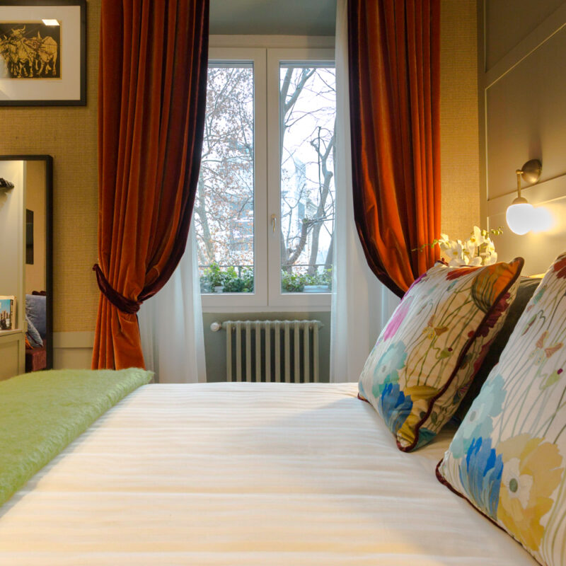 Suite con letto, coprilettoi bianco, cuscini stampa floreale, finestra con vista sugli alberi